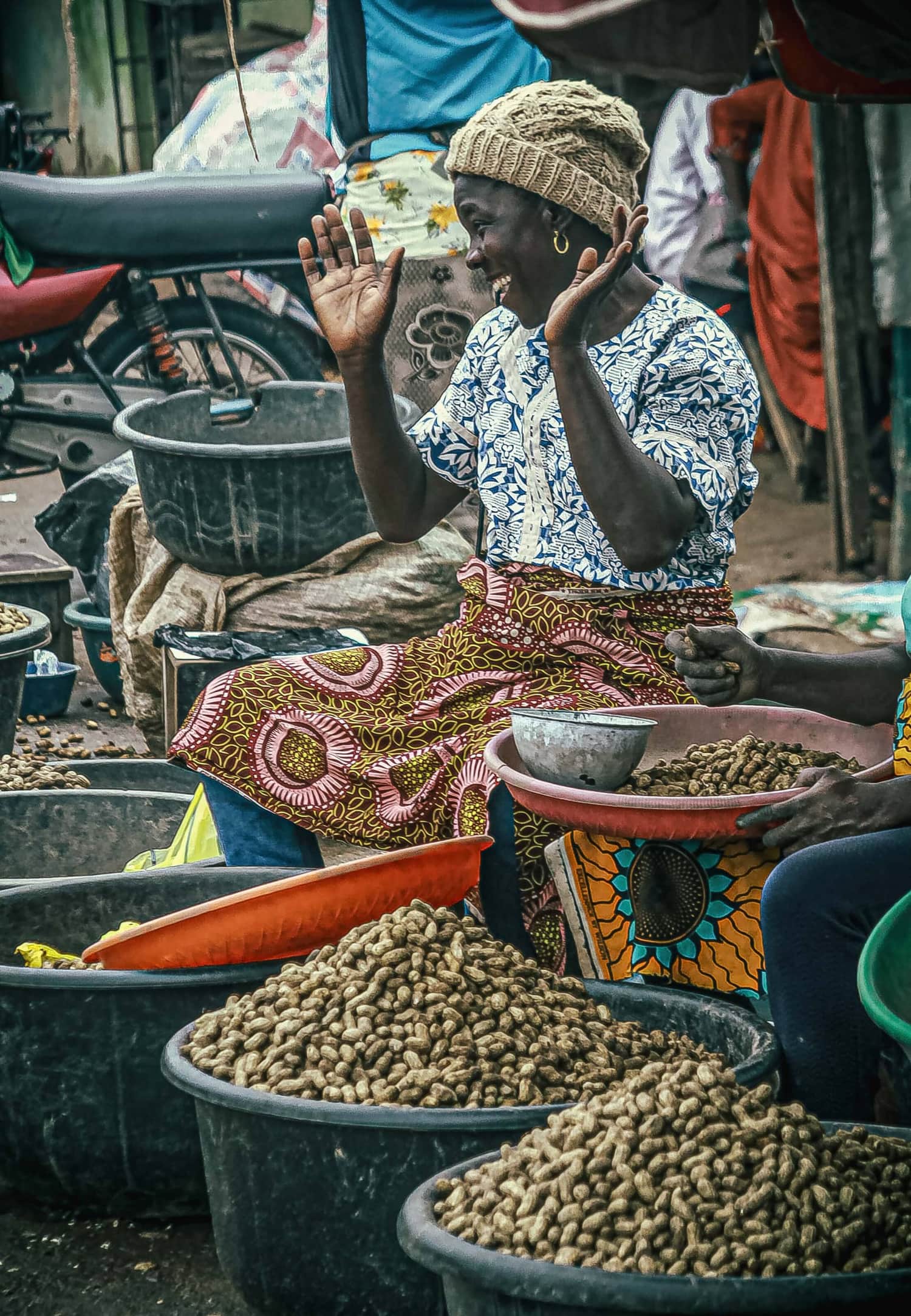 A Nigerian trader laughing while selling groundnuts at a market